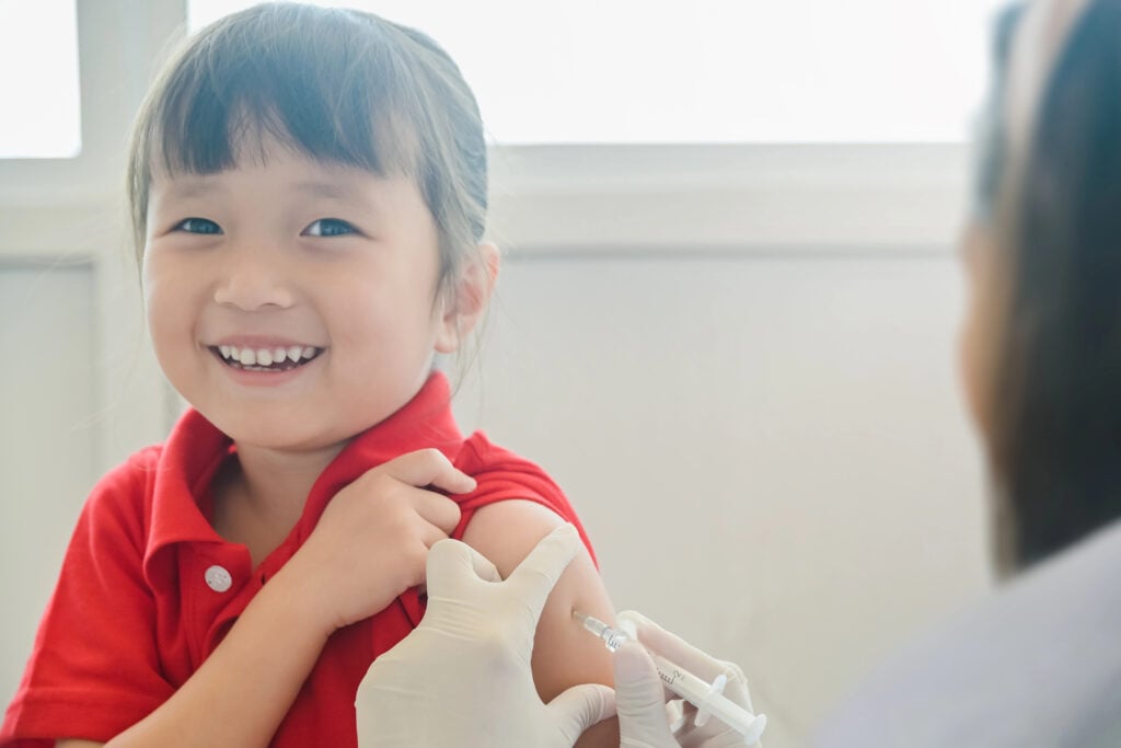 Asian Little child having Injection,Close-up Doctor injecting vaccination to arm of little girl her smile face and looking camera ,vaccine injection for immunization health and medical concept.