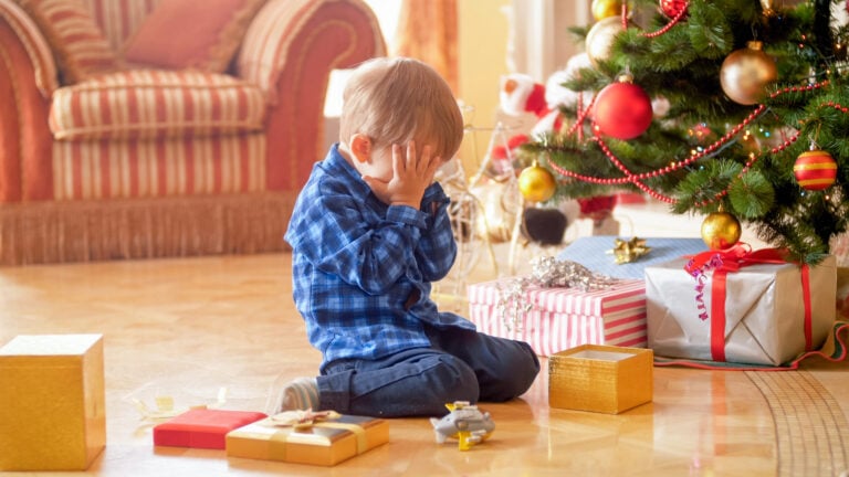 Little toddler boy sitting under Christmas tree and crying
