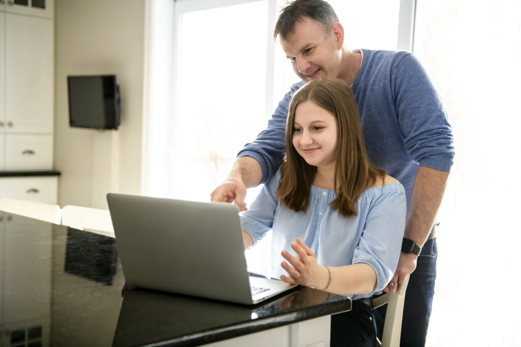 A father using a laptop in kitchen with teenager