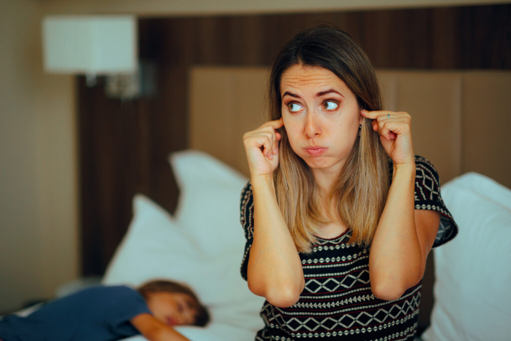 Woman Covering her Ears while her Toddler Snores during Nap
