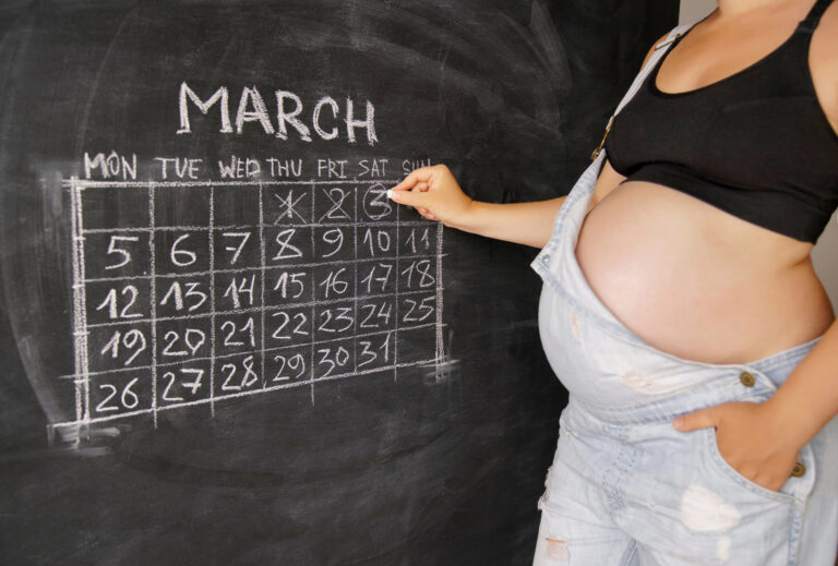 The concept of pregnancy. Young pregnant woman counting days with a calendar for the birth of a child on a chalkboard