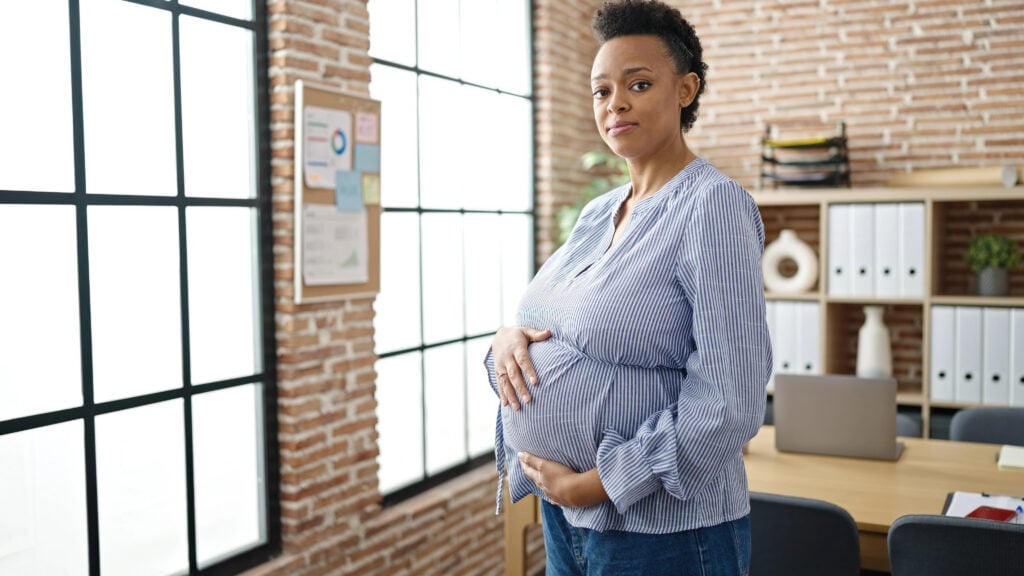 Young pregnant woman business worker touching belly with serious expression at office