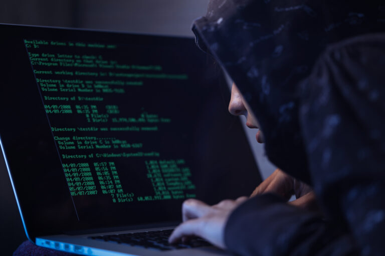 Computer hacker in hooded shirt typing software algorithms and stealing data from computer network on laptop.