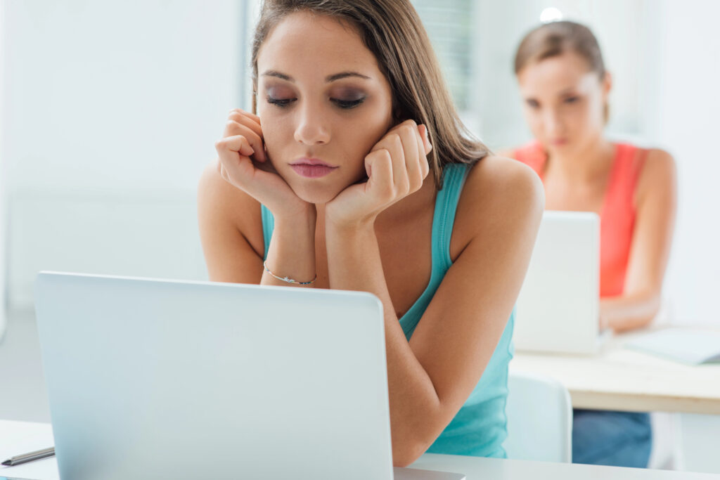 A teen is using the computer while looking unhappy